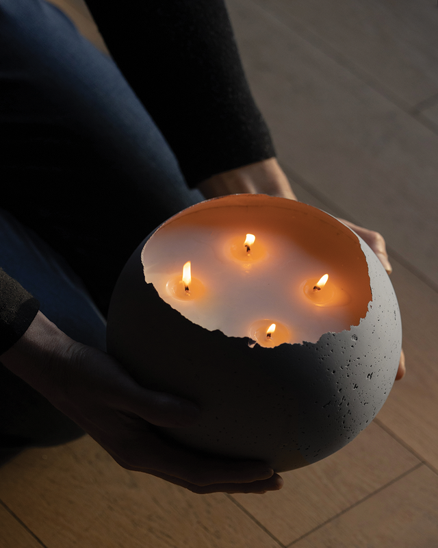 A person holding a round concrete candle with four lit wicks, showcasing the subtle bright citrus scent.