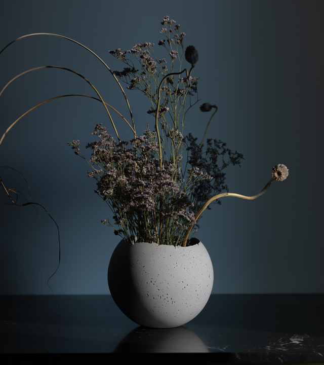 Hand-crafted concrete vessel with a live-edge opening, in a natural gray color with a dried floral arrangement