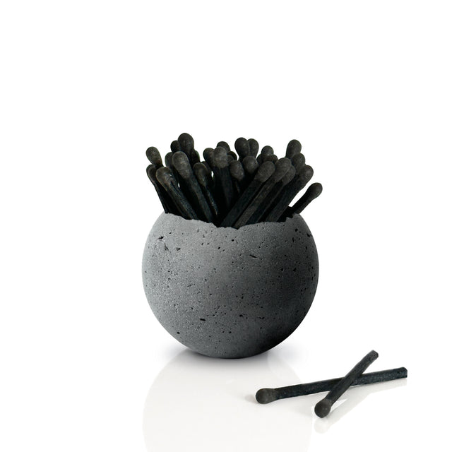A gray concrete Orbis vessel with a round shape, displaying a collection of black matches, on a white background.