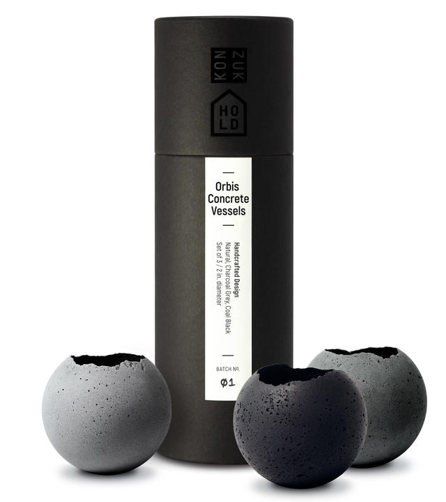 Three Orbis concrete vessels of different shades of grey, presented next to their custom black packaging tube.