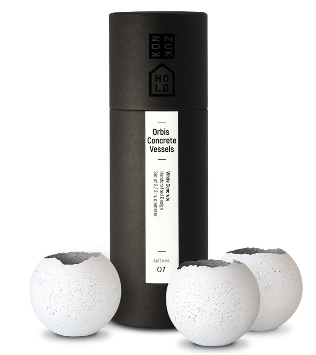 Three white concrete spherical vessels of varying sizes, presented with a custom black packaging tube labeled 'Orbis Concrete Vessels'.