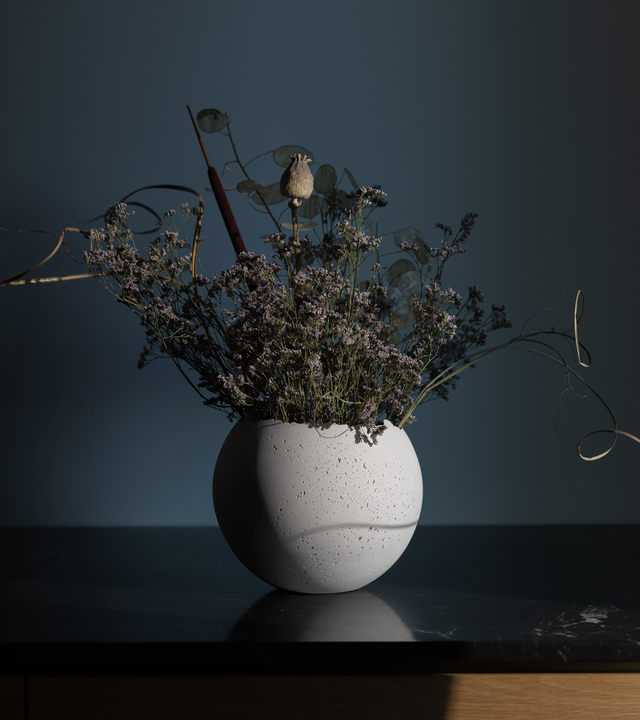 Hand-crafted white-tinted concrete vessel with a live-edge opening, showcasing a unique, fragmented geometric shape with dried floral arrangement