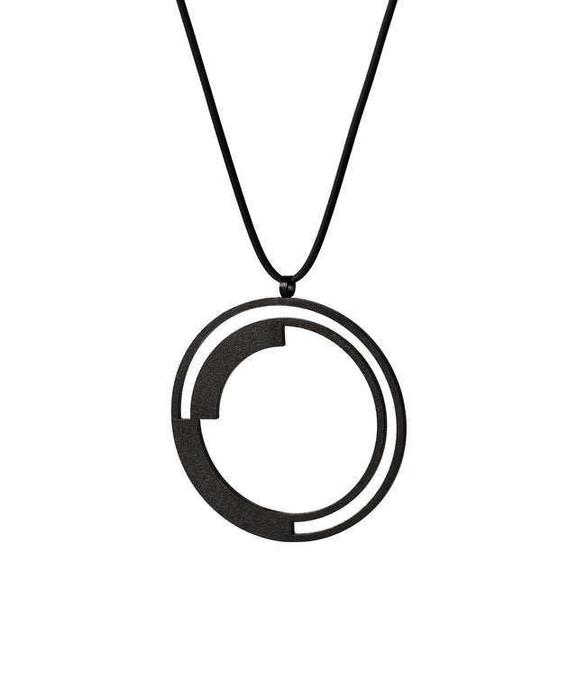 side view of This pendant introduces curves into the collection's vocabulary, creating a rhythmic balance as the solid forms anchor the circular form while leaving generous arcs of openness between them. The double-ring structure adds depth and layering, transforming the simple circle into a study of rotation and counterbalance. It's a dynamic composition that suggests movement and continuity, as if the solid arcs are in gentle orbit within their circular bounds.
