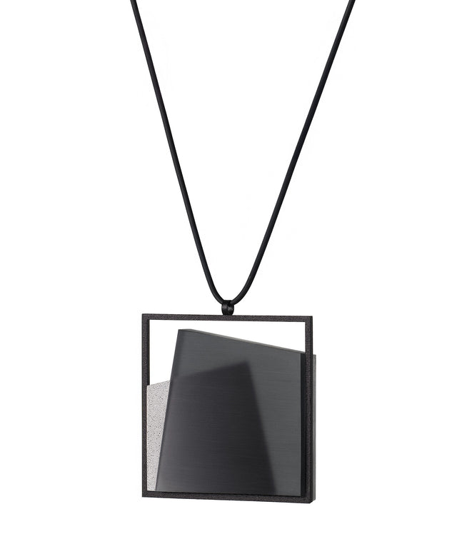 The Astrid necklace in ash grey takes its name from Old Norse, meaning “divinely beautiful,” a reflection of its quiet, sculptural presence. Within the square frame, concrete intersects with resin in a deliberate composition that reveals depth and movement. The meeting of materials creates subtle shifts in tone and surface, drawing the eye to the balance between precision and softness.