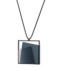 side view of The Astrid necklace in cerulean blue takes its name from Old Norse, meaning “divinely beautiful,” a reflection of its quiet, sculptural presence. Within the square frame, concrete intersects with resin in a deliberate composition that reveals depth and movement. The meeting of materials creates subtle shifts in tone and surface, drawing the eye to the balance between precision and softness. The Astrid necklace embodies refined minimalism with a sense of calm, architectural beauty.