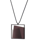 side view of The Astrid necklace in cognac takes its name from Old Norse, meaning “divinely beautiful,” a reflection of its quiet, sculptural presence. Within the square frame, concrete intersects with resin in a deliberate composition that reveals depth and movement. The meeting of materials creates subtle shifts in tone and surface, drawing the eye to the balance between precision and softness. The Astrid necklace embodies refined minimalism with a sense of calm, architectural beauty.