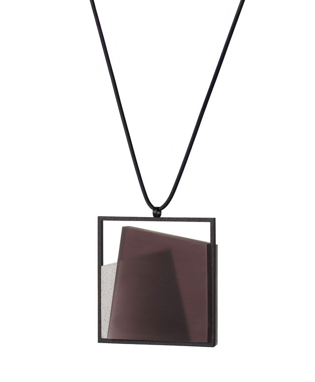 side view of The Astrid necklace in cognac takes its name from Old Norse, meaning “divinely beautiful,” a reflection of its quiet, sculptural presence. Within the square frame, concrete intersects with resin in a deliberate composition that reveals depth and movement. The meeting of materials creates subtle shifts in tone and surface, drawing the eye to the balance between precision and softness. The Astrid necklace embodies refined minimalism with a sense of calm, architectural beauty.
