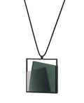 side view of The Astrid necklace in cypress green takes its name from Old Norse, meaning “divinely beautiful,” a reflection of its quiet, sculptural presence. Within the square frame, concrete intersects with resin in a deliberate composition that reveals depth and movement. The meeting of materials creates subtle shifts in tone and surface, drawing the eye to the balance between precision and softness.