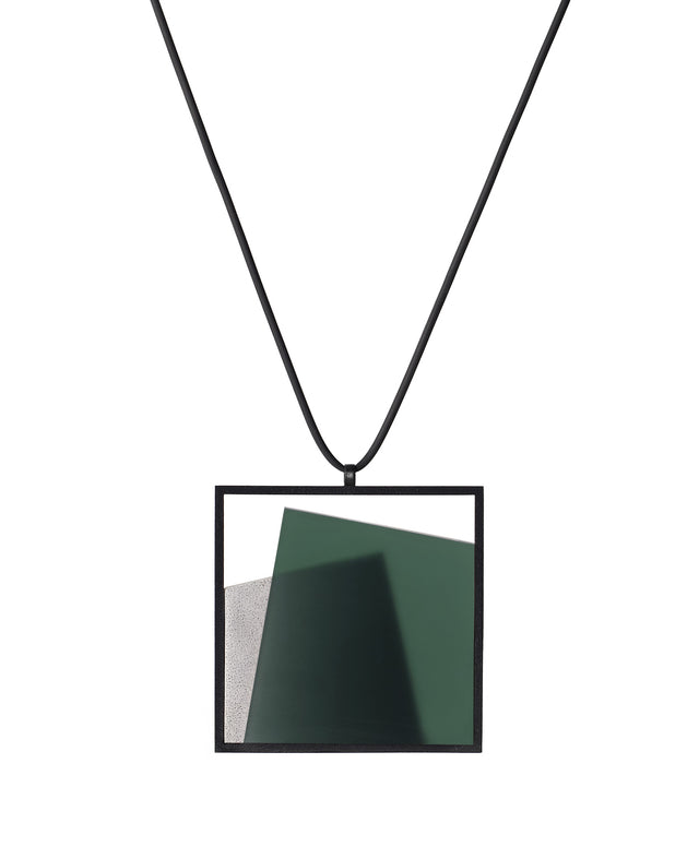 The Astrid necklace in cypress green takes its name from Old Norse, meaning “divinely beautiful,” a reflection of its quiet, sculptural presence. Within the square frame, concrete intersects with resin in a deliberate composition that reveals depth and movement. The meeting of materials creates subtle shifts in tone and surface, drawing the eye to the balance between precision and softness.