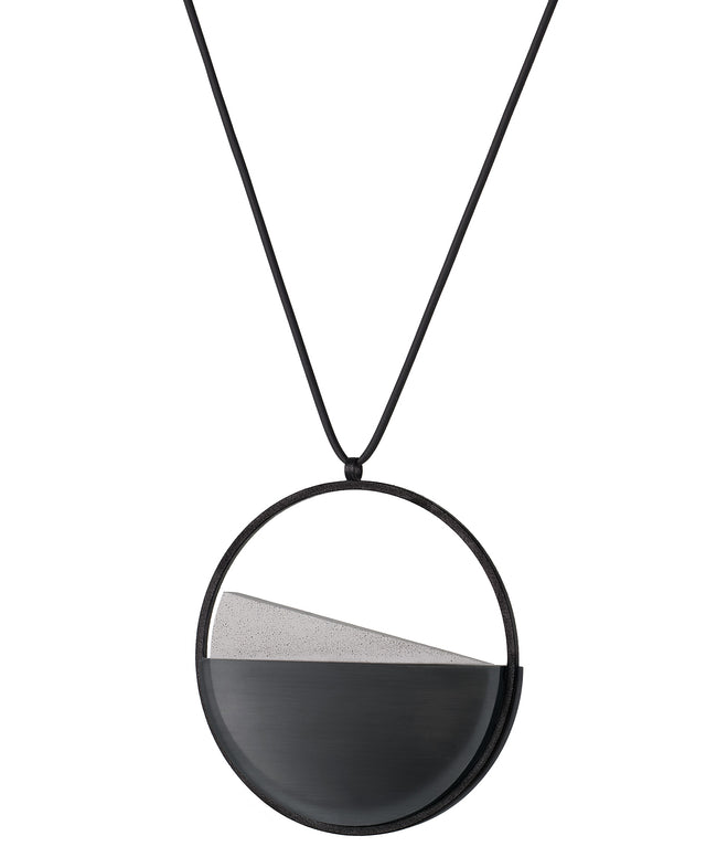 side version of the Clara necklace in ash grey embodies clarity and balance. Named from the Latin clarus, meaning “bright” or “clear,” it reflects the quiet harmony of light and material. Within the circular frame, concrete emerges from the surface of the resin, creating a gentle rise in tone and texture. The Clara necklace carries a calm, sculptural presence that feels both modern and enduring.