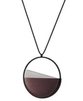 side view of the Clara necklace in cognac resin embodies clarity and balance. Named from the Latin clarus, meaning “bright” or “clear,” it reflects the quiet harmony of light and material. Within the circular frame, concrete emerges from the surface of the resin, creating a gentle rise in tone and texture. The Clara necklace carries a calm, sculptural presence that feels both modern and enduring.