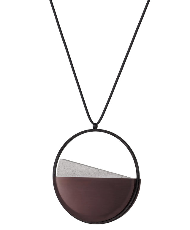 side view of the Clara necklace in cognac resin embodies clarity and balance. Named from the Latin clarus, meaning “bright” or “clear,” it reflects the quiet harmony of light and material. Within the circular frame, concrete emerges from the surface of the resin, creating a gentle rise in tone and texture. The Clara necklace carries a calm, sculptural presence that feels both modern and enduring.