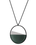 side view of The Clara necklace in cypress green resin embodies clarity and balance. Named from the Latin clarus, meaning “bright” or “clear,” it reflects the quiet harmony of light and material. Within the circular frame, concrete emerges from the surface of the resin, creating a gentle rise in tone and texture. The Clara necklace carries a calm, sculptural presence that feels both modern and enduring.