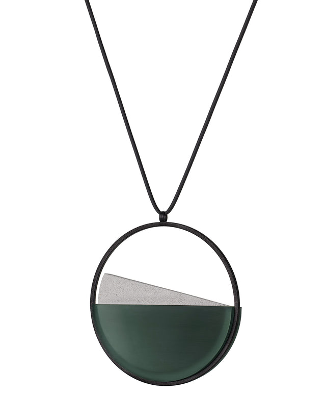 side view of The Clara necklace in cypress green resin embodies clarity and balance. Named from the Latin clarus, meaning “bright” or “clear,” it reflects the quiet harmony of light and material. Within the circular frame, concrete emerges from the surface of the resin, creating a gentle rise in tone and texture. The Clara necklace carries a calm, sculptural presence that feels both modern and enduring.