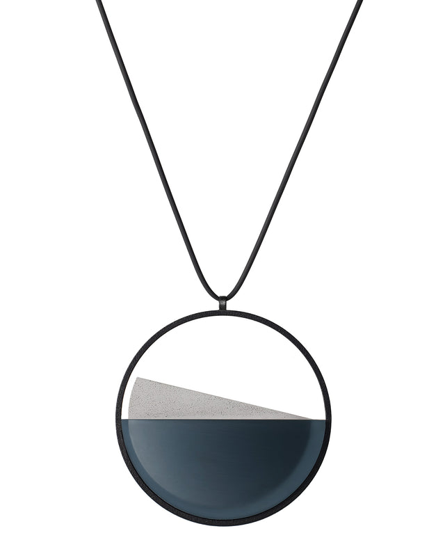 The Clara necklace in cerulean blue embodies clarity and balance. Named from the Latin clarus, meaning “bright” or “clear,” it reflects the quiet harmony of light and material. Within the circular frame, concrete emerges from the surface of the resin, creating a gentle rise in tone and texture. The Clara necklace carries a calm, sculptural presence that feels both modern and enduring.