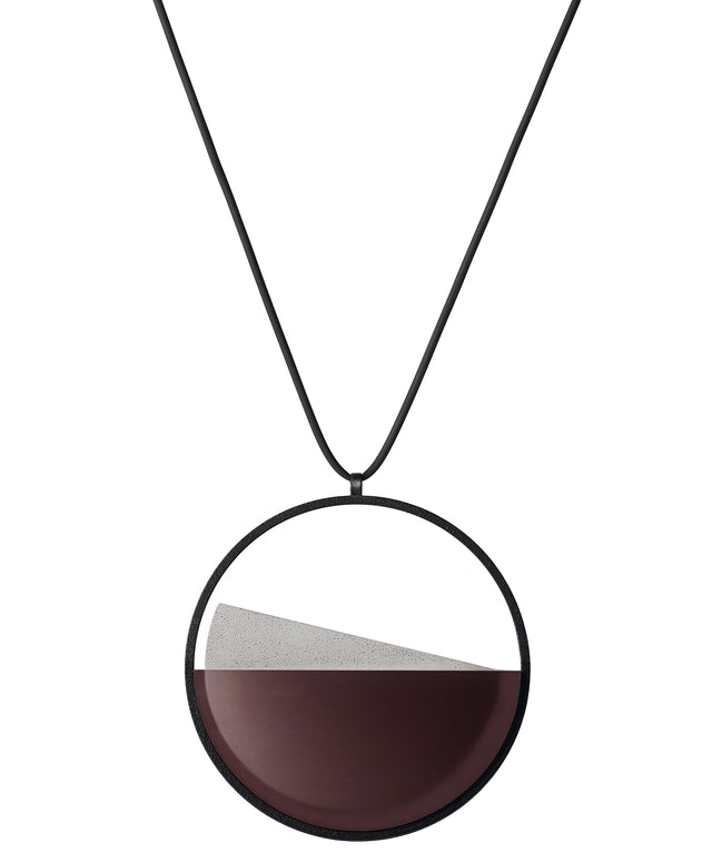The Clara necklace in cognac resin embodies clarity and balance. Named from the Latin clarus, meaning “bright” or “clear,” it reflects the quiet harmony of light and material. Within the circular frame, concrete emerges from the surface of the resin, creating a gentle rise in tone and texture. The Clara necklace carries a calm, sculptural presence that feels both modern and enduring.