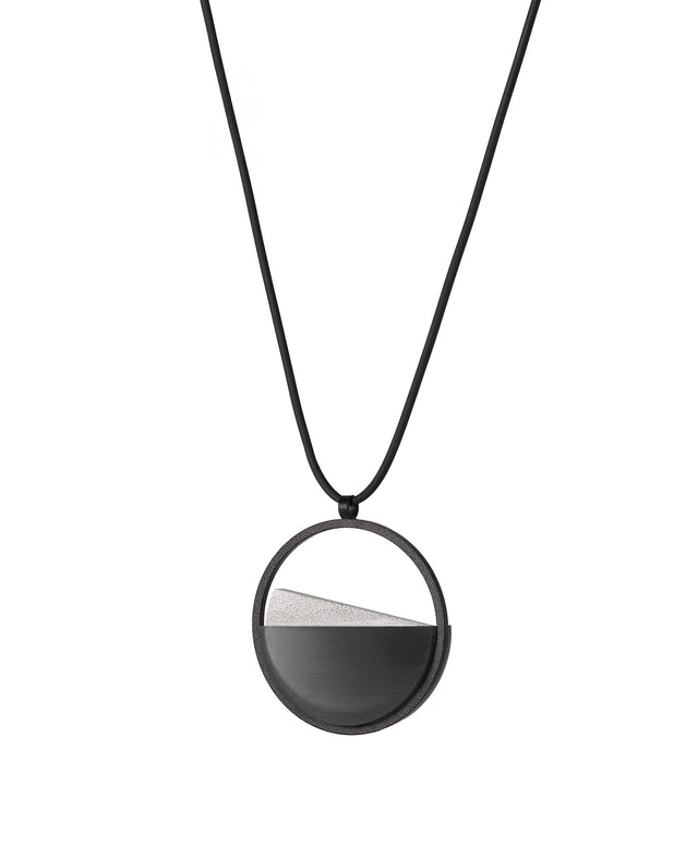 side view of The Clara Small necklace in Ash grey resin captures the essence of clarity in a refined, understated form. Named from the Latin clarus, meaning “bright” or “clear,” it reveals a quiet balance between resin and concrete. Within the circular frame, the concrete emerges gently from the resin’s surface, creating a soft meeting of tone and texture. 