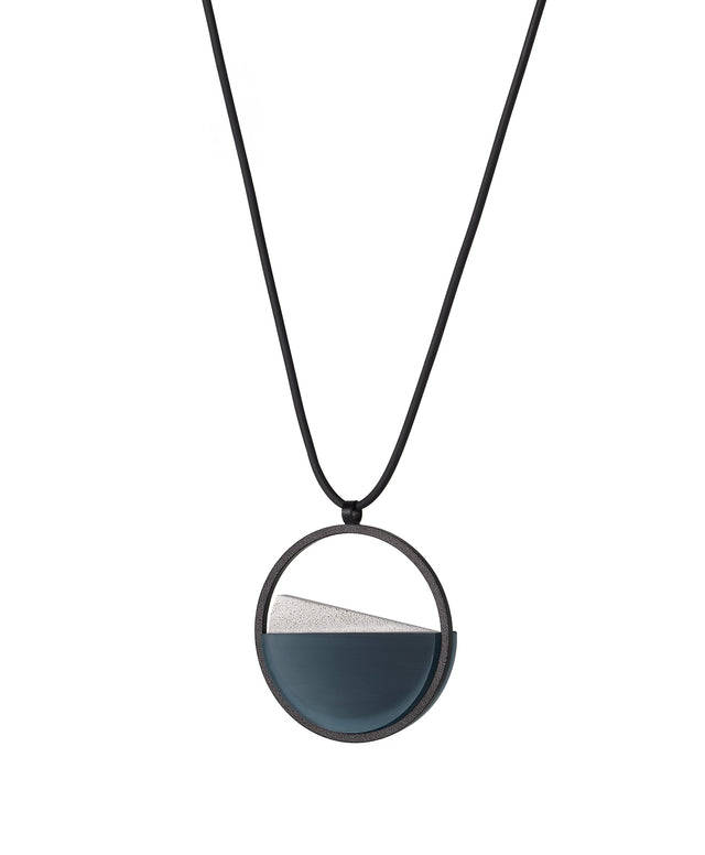 side view of The Clara Small necklace in cerulean blue resin captures the essence of clarity in a refined, understated form. Named from the Latin clarus, meaning “bright” or “clear,” it reveals a quiet balance between resin and concrete. Within the circular frame, the concrete emerges gently from the resin’s surface, creating a soft meeting of tone and texture. 