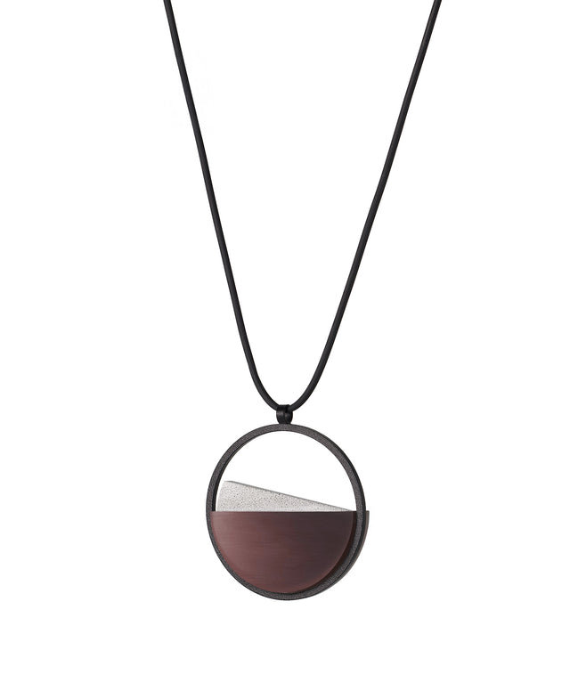 side view of The Clara Small necklace in cognac grey resin captures the essence of clarity in a refined, understated form. Named from the Latin clarus, meaning “bright” or “clear,” it reveals a quiet balance between resin and concrete. Within the circular frame, the concrete emerges gently from the resin’s surface, creating a soft meeting of tone and texture. 