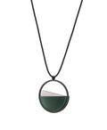 side view of The Clara Small necklace in Cypress green resin captures the essence of clarity in a refined, understated form. Named from the Latin clarus, meaning “bright” or “clear,” it reveals a quiet balance between resin and concrete. Within the circular frame, the concrete emerges gently from the resin’s surface, creating a soft meeting of tone and texture. 