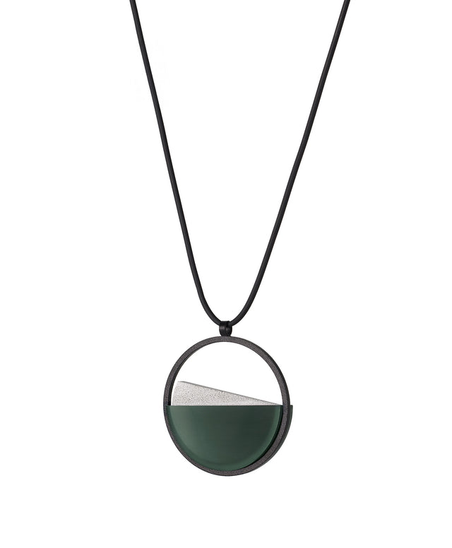 side view of The Clara Small necklace in Cypress green resin captures the essence of clarity in a refined, understated form. Named from the Latin clarus, meaning “bright” or “clear,” it reveals a quiet balance between resin and concrete. Within the circular frame, the concrete emerges gently from the resin’s surface, creating a soft meeting of tone and texture. 