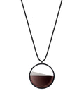 The Clara Small necklace in cognac resin captures the essence of clarity in a refined, understated form. Named from the Latin clarus, meaning “bright” or “clear,” it reveals a quiet balance between resin and concrete. Within the circular frame, the concrete emerges gently from the resin’s surface, creating a soft meeting of tone and texture. 