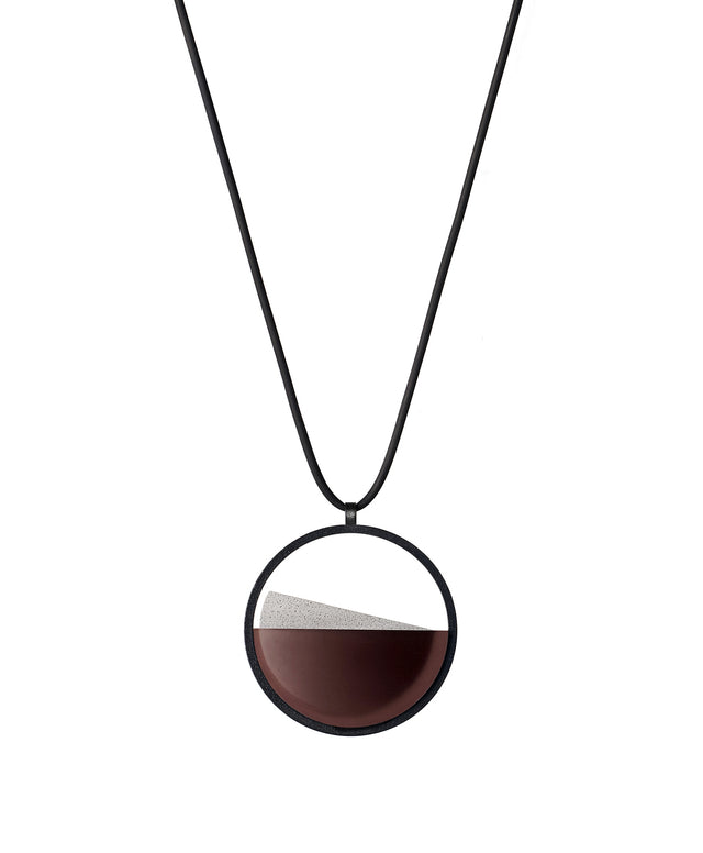 The Clara Small necklace in cognac resin captures the essence of clarity in a refined, understated form. Named from the Latin clarus, meaning “bright” or “clear,” it reveals a quiet balance between resin and concrete. Within the circular frame, the concrete emerges gently from the resin’s surface, creating a soft meeting of tone and texture. 