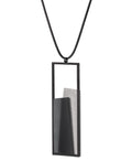 Side view of The Eira necklace in Ash grey brings together concrete and resin in a seamless composition that highlights material depth and subtle tone. Within the black rectangular frame, the concrete appears softly suspended in resin, giving the piece a quiet sense of balance and dimension. The surface catches light in a gentle, diffused way, creating an effect that feels both grounded and luminous. The Eira necklace offers a refined expression of modern minimalism.