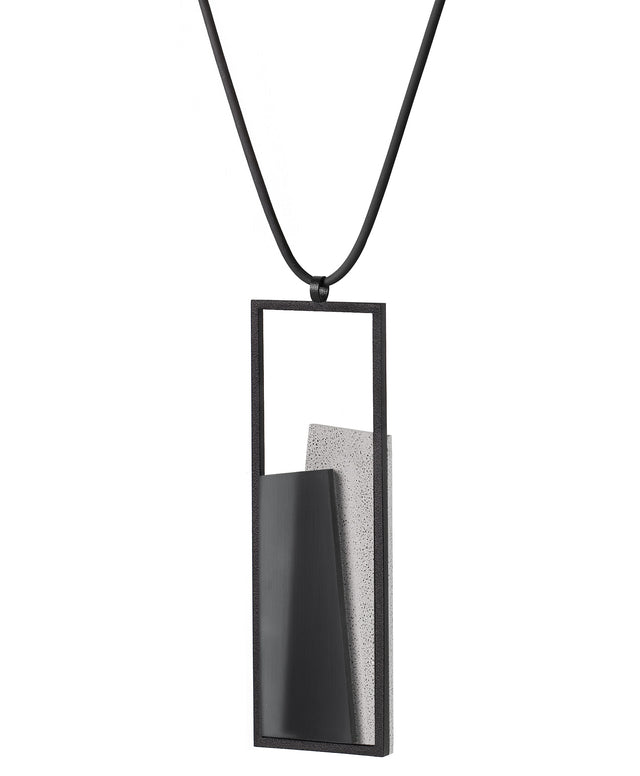 Side view of The Eira necklace in Ash grey brings together concrete and resin in a seamless composition that highlights material depth and subtle tone. Within the black rectangular frame, the concrete appears softly suspended in resin, giving the piece a quiet sense of balance and dimension. The surface catches light in a gentle, diffused way, creating an effect that feels both grounded and luminous. The Eira necklace offers a refined expression of modern minimalism.
