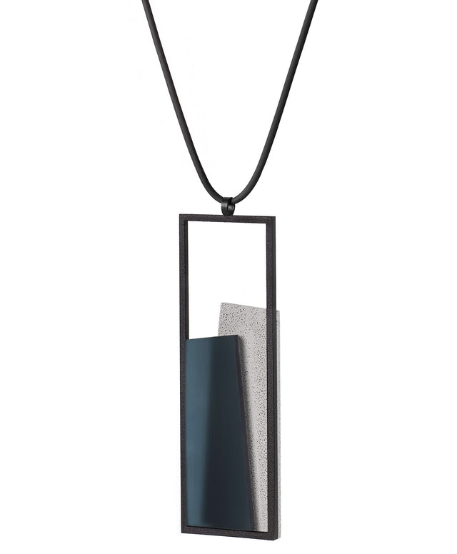 Side view of The Eira necklace in Cerulean Blue brings together concrete and resin in a seamless composition that highlights material depth and subtle tone. Within the black rectangular frame, the concrete appears softly suspended in resin, giving the piece a quiet sense of balance and dimension. The surface catches light in a gentle, diffused way, creating an effect that feels both grounded and luminous. The Eira necklace offers a refined expression of modern minimalism.