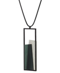 side view of The Eira necklace  in Cypress Green brings together concrete and resin in a seamless composition that highlights material depth and subtle tone. Within the black rectangular frame, the concrete appears softly suspended in resin, giving the piece a quiet sense of balance and dimension. The surface catches light in a gentle, diffused way, creating an effect that feels both grounded and luminous. The Eira necklace offers a refined expression of modern minimalism.