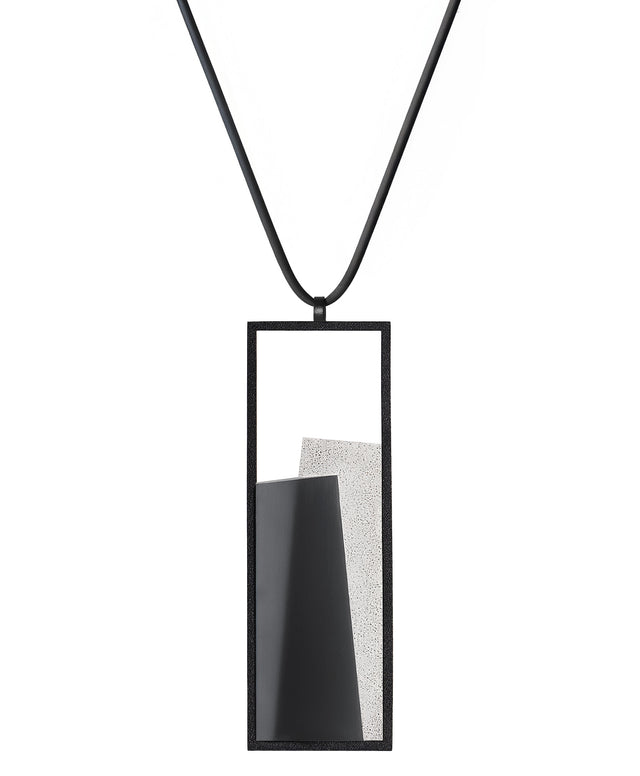 The Eira necklace in Ash grey brings together concrete and resin in a seamless composition that highlights material depth and subtle tone. Within the black rectangular frame, the concrete appears softly suspended in resin, giving the piece a quiet sense of balance and dimension. The surface catches light in a gentle, diffused way, creating an effect that feels both grounded and luminous. The Eira necklace offers a refined expression of modern minimalism.
