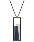 The Eira necklace in Cerulean blue brings together concrete and resin in a seamless composition that highlights material depth and subtle tone. Within the black rectangular frame, the concrete appears softly suspended in resin, giving the piece a quiet sense of balance and dimension. The surface catches light in a gentle, diffused way, creating an effect that feels both grounded and luminous. The Eira necklace offers a refined expression of modern minimalism.