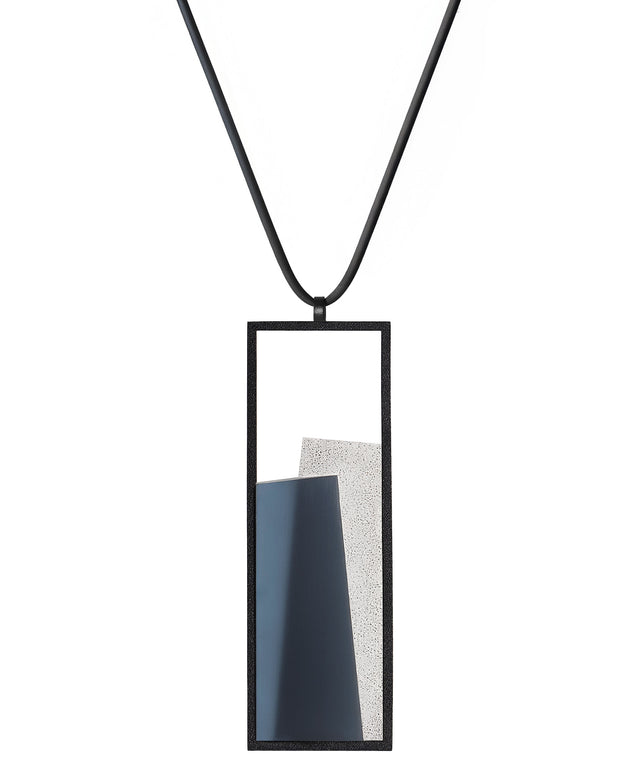 The Eira necklace in Cerulean blue brings together concrete and resin in a seamless composition that highlights material depth and subtle tone. Within the black rectangular frame, the concrete appears softly suspended in resin, giving the piece a quiet sense of balance and dimension. The surface catches light in a gentle, diffused way, creating an effect that feels both grounded and luminous. The Eira necklace offers a refined expression of modern minimalism.