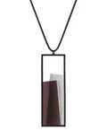 The Eira necklace in Cognac resin brings together concrete and resin in a seamless composition that highlights material depth and subtle tone. Within the black rectangular frame, the concrete appears softly suspended in resin, giving the piece a quiet sense of balance and dimension. The surface catches light in a gentle, diffused way, creating an effect that feels both grounded and luminous. The Eira necklace offers a refined expression of modern minimalism.