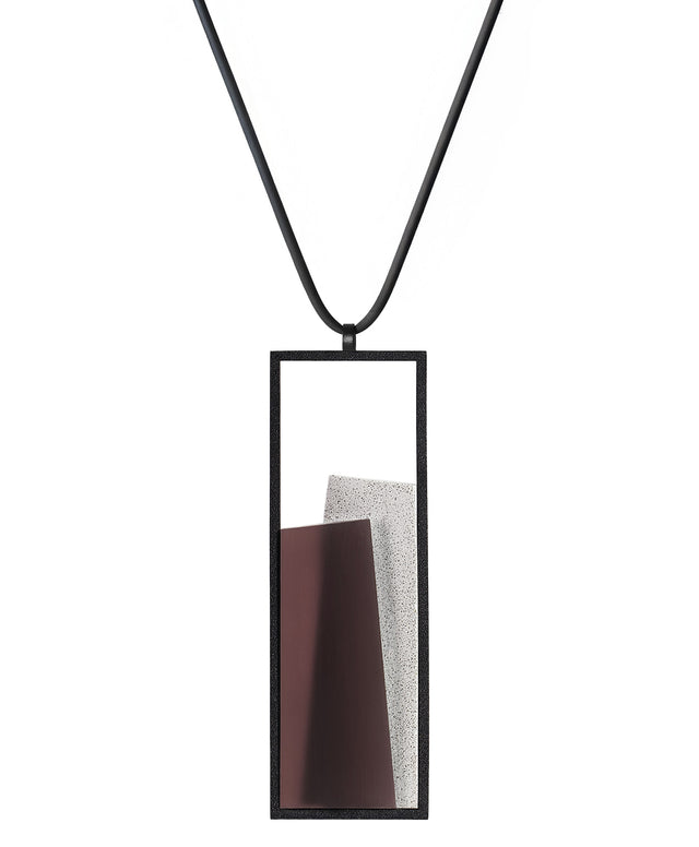 The Eira necklace in Cognac resin brings together concrete and resin in a seamless composition that highlights material depth and subtle tone. Within the black rectangular frame, the concrete appears softly suspended in resin, giving the piece a quiet sense of balance and dimension. The surface catches light in a gentle, diffused way, creating an effect that feels both grounded and luminous. The Eira necklace offers a refined expression of modern minimalism.