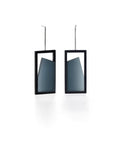 The Elena earrings play with light through a sleek, elongated form. A vertical resin plane reveals a smooth gradient that shifts from light to shadow, bringing subtle movement to the piece. The translucent resin captures and softens light, creating a quiet glow within the structured black frame. Modern and understated, these earrings offer a refined balance of geometry and fluid luminosity. in cerulean blue