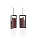 The Elena earrings play with light through a sleek, elongated form. A vertical resin plane reveals a smooth gradient that shifts from light to shadow, bringing subtle movement to the piece. The translucent resin captures and softens light, creating a quiet glow within the structured black frame. Modern and understated, these earrings offer a refined balance of geometry and fluid luminosity. in cognac