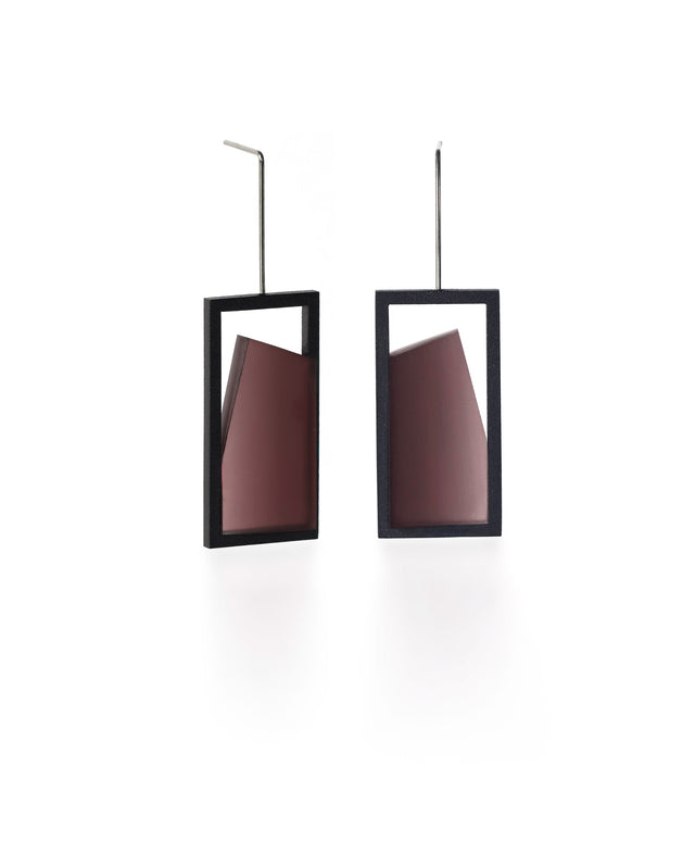 The Elena earrings play with light through a sleek, elongated form. A vertical resin plane reveals a smooth gradient that shifts from light to shadow, bringing subtle movement to the piece. The translucent resin captures and softens light, creating a quiet glow within the structured black frame. Modern and understated, these earrings offer a refined balance of geometry and fluid luminosity. in cognac