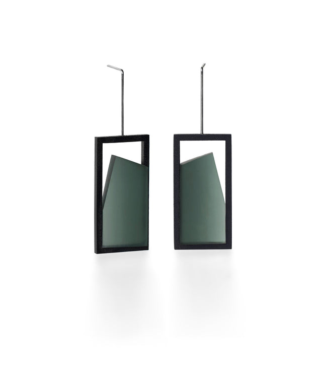 The Elena earrings play with light through a sleek, elongated form. A vertical resin plane reveals a smooth gradient that shifts from light to shadow, bringing subtle movement to the piece. The translucent resin captures and softens light, creating a quiet glow within the structured black frame. Modern and understated, these earrings offer a refined balance of geometry and fluid luminosity. in cypress green