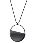 The side view of The Vestra necklace in Ash grey embodies balance and quiet strength. Its name, derived from the Latin vestra, meaning “yours,” speaks to a personal connection between wearer and form. Within the circular frame, concrete is cast into resin revealing a smooth plane of depth and tone, reflecting light in a soft, fluid way. The composition feels calm and grounded, offering a sculptural presence that becomes uniquely individual when worn.