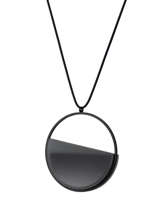The side view of The Vestra necklace in Ash grey embodies balance and quiet strength. Its name, derived from the Latin vestra, meaning “yours,” speaks to a personal connection between wearer and form. Within the circular frame, concrete is cast into resin revealing a smooth plane of depth and tone, reflecting light in a soft, fluid way. The composition feels calm and grounded, offering a sculptural presence that becomes uniquely individual when worn.