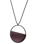 side view of The Vestra necklace in Cognac resin embodies balance and quiet strength. Its name, derived from the Latin vestra, meaning “yours,” speaks to a personal connection between wearer and form. Within the circular frame, concrete is cast into resin revealing a smooth plane of depth and tone, reflecting light in a soft, fluid way. The composition feels calm and grounded, offering a sculptural presence that becomes uniquely individual when worn.