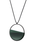 Side view of The Vestra necklace in Cypress green resin embodies balance and quiet strength. Its name, derived from the Latin vestra, meaning “yours,” speaks to a personal connection between wearer and form. Within the circular frame, concrete is cast into resin revealing a smooth plane of depth and tone, reflecting light in a soft, fluid way. The composition feels calm and grounded, offering a sculptural presence that becomes uniquely individual when worn.