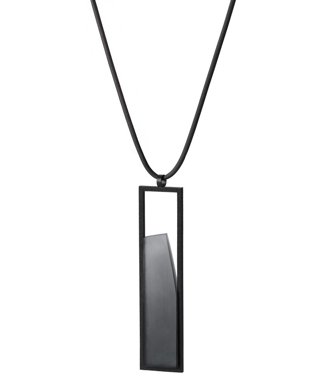 side view of The Lucia necklace in Ash grey resin features a sleek rectangular pendant that emphasizes form and material. A cast resin element rests within a black frame, creating a sense of depth and quiet luminosity. The elongated shape draws the eye, offering a refined balance between structure and softness. Minimal and striking, the Lucia necklace adds a sculptural accent that complements both everyday and statement looks.