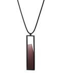 side view of The Lucia necklace in Cognac resin features a sleek rectangular pendant that emphasizes form and material. A cast resin element rests within a black frame, creating a sense of depth and quiet luminosity. The elongated shape draws the eye, offering a refined balance between structure and softness. Minimal and striking, the Lucia necklace adds a sculptural accent that complements both everyday and statement looks.