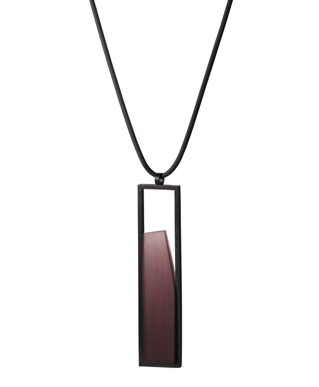 side view of The Lucia necklace in Cognac resin features a sleek rectangular pendant that emphasizes form and material. A cast resin element rests within a black frame, creating a sense of depth and quiet luminosity. The elongated shape draws the eye, offering a refined balance between structure and softness. Minimal and striking, the Lucia necklace adds a sculptural accent that complements both everyday and statement looks.