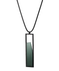 side view of The Lucia necklace in Cypress green  resin features a sleek rectangular pendant that emphasizes form and material. A cast resin element rests within a black frame, creating a sense of depth and quiet luminosity. The elongated shape draws the eye, offering a refined balance between structure and softness. Minimal and striking, the Lucia necklace adds a sculptural accent that complements both everyday and statement looks.