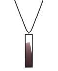 The Lucia necklace in Cognac resin features a sleek rectangular pendant that emphasizes form and material. A cast resin element rests within a black frame, creating a sense of depth and quiet luminosity. The elongated shape draws the eye, offering a refined balance between structure and softness. Minimal and striking, the Lucia necklace adds a sculptural accent that complements both everyday and statement looks.