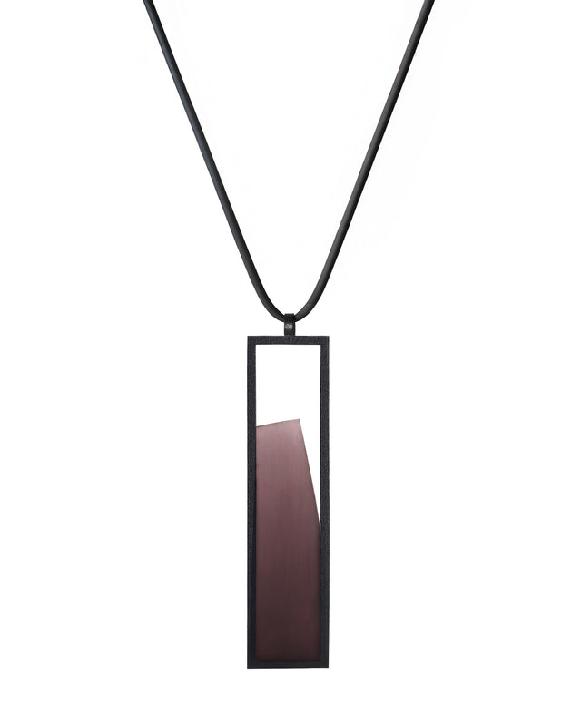 The Lucia necklace in Cognac resin features a sleek rectangular pendant that emphasizes form and material. A cast resin element rests within a black frame, creating a sense of depth and quiet luminosity. The elongated shape draws the eye, offering a refined balance between structure and softness. Minimal and striking, the Lucia necklace adds a sculptural accent that complements both everyday and statement looks.
